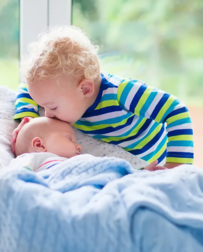 Toddler kissing a newborn baby