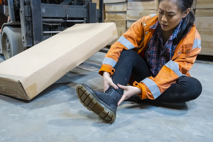 Warehouse worker sitting on the floor holding an injured ankle